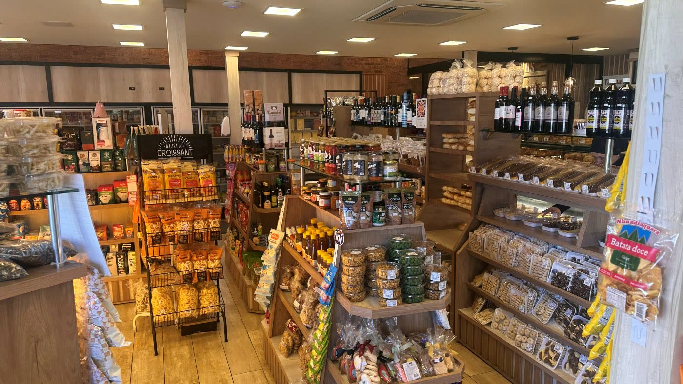 Interior da loja com estantes de biscoitos, geleias, vinhos e produtos coloniais